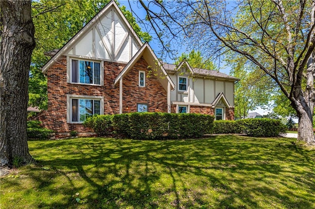 tudor home with brick siding, a front lawn, and stucco siding