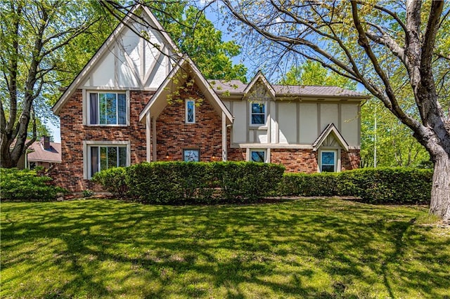 tudor home featuring stucco siding, brick siding, and a front yard