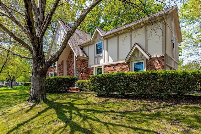 tudor-style house featuring stucco siding, brick siding, and a front yard