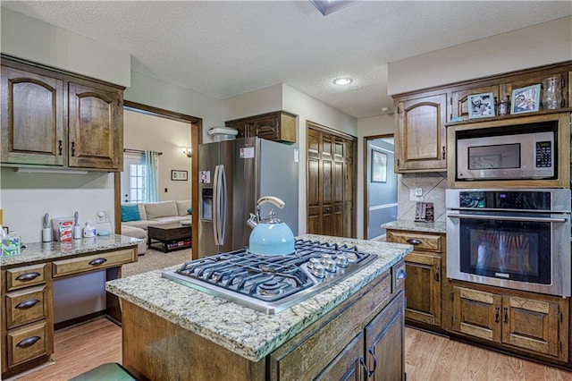 kitchen with appliances with stainless steel finishes, light wood-type flooring, a textured ceiling, light stone countertops, and a center island
