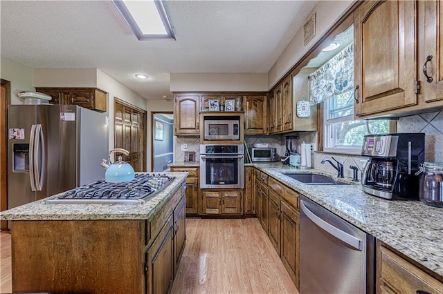 kitchen with appliances with stainless steel finishes, light wood finished floors, a sink, light stone counters, and decorative backsplash