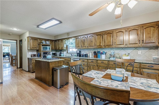 kitchen featuring stainless steel microwave, brown cabinets, a sink, a ceiling fan, and backsplash