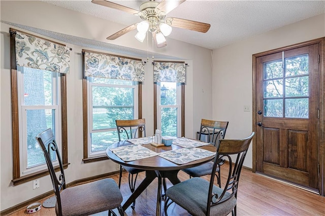 dining space with plenty of natural light, light wood-style floors, a textured ceiling, a ceiling fan, and baseboards