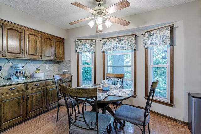 dining space featuring light wood finished floors, plenty of natural light, a ceiling fan, a textured ceiling, and baseboards