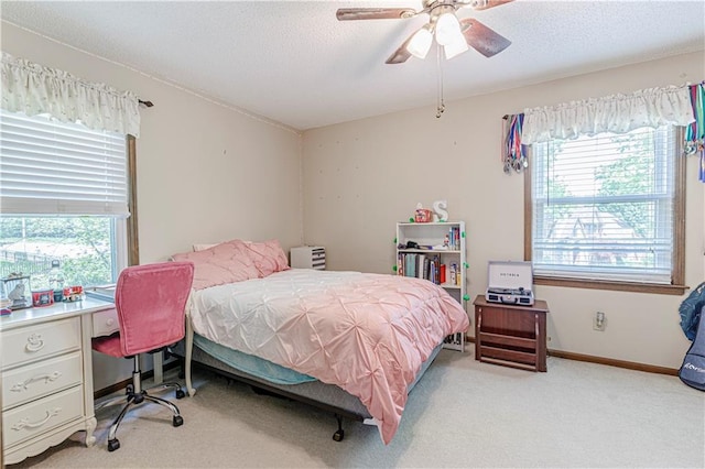 bedroom featuring multiple windows, light carpet, baseboards, an office area, and a textured ceiling