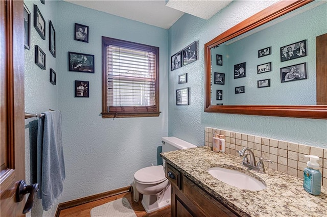 half bath featuring a textured wall, wood finished floors, backsplash, toilet, and vanity