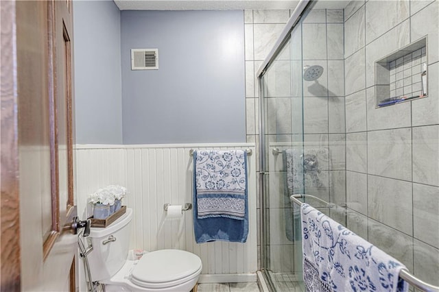 full bathroom featuring toilet, a shower stall, and wainscoting