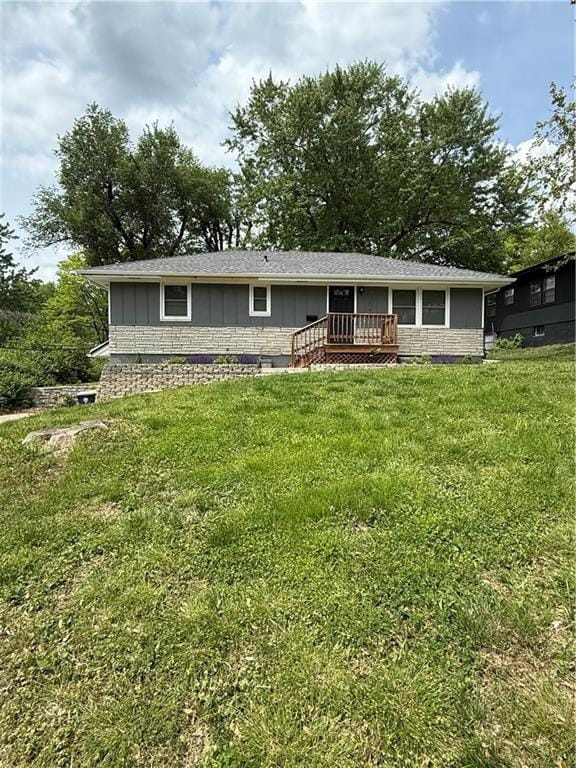 single story home with board and batten siding, a front lawn, stone siding, and a deck