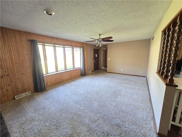 unfurnished room with ceiling fan, wood walls, carpet flooring, and a textured ceiling