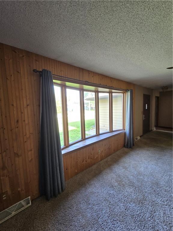 carpeted spare room featuring plenty of natural light, wood walls, and a textured ceiling