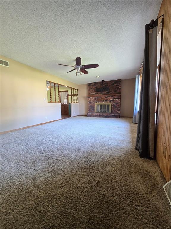 unfurnished living room with carpet floors, a ceiling fan, a fireplace, a textured ceiling, and baseboards