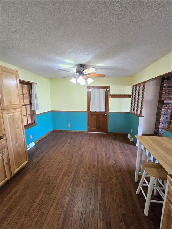 unfurnished dining area with dark wood-type flooring, ceiling fan, a textured ceiling, baseboards, and a wainscoted wall