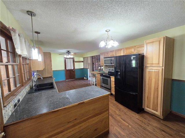 kitchen featuring stainless steel appliances, a sink, dark wood-style flooring, dark countertops, and a chandelier