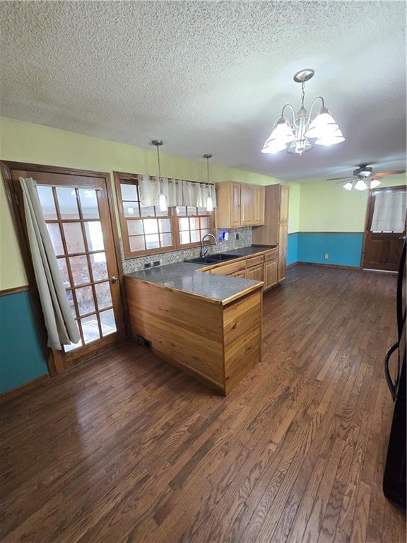 kitchen featuring a peninsula, a textured ceiling, dark wood-style floors, a chandelier, and a sink
