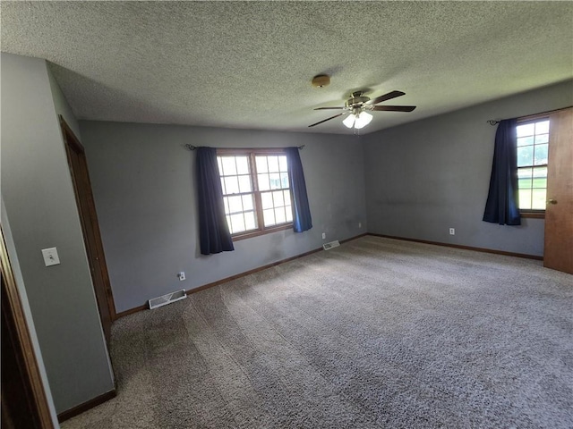 carpeted empty room with ceiling fan, plenty of natural light, baseboards, and a textured ceiling