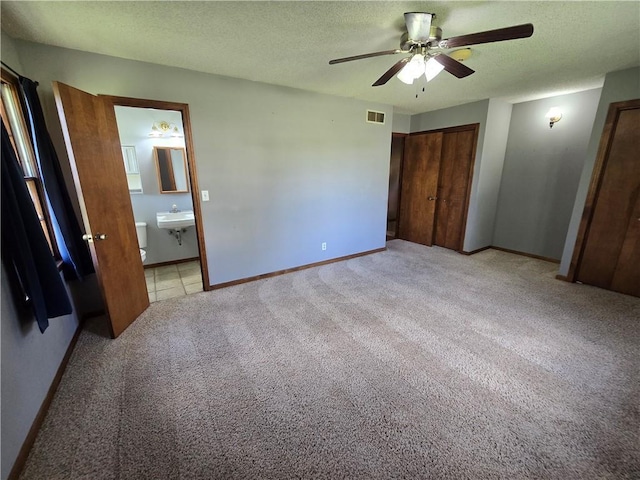 unfurnished bedroom with light colored carpet, baseboards, ensuite bathroom, ceiling fan, and a textured ceiling