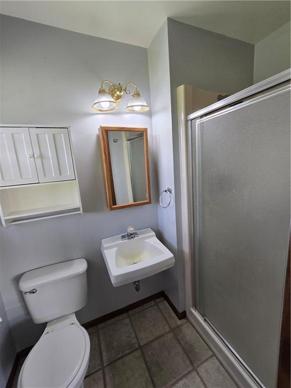 full bathroom with a sink, a shower stall, toilet, and baseboards