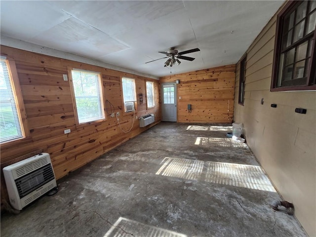 unfurnished living room featuring heating unit, a wall unit AC, wood walls, a ceiling fan, and cooling unit
