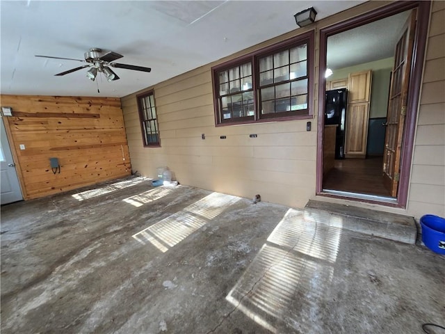 unfurnished living room featuring wood walls, a ceiling fan, and concrete flooring
