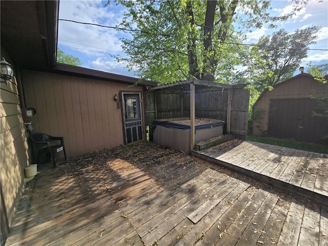 wooden deck featuring a hot tub, an outbuilding, a storage unit, and fence