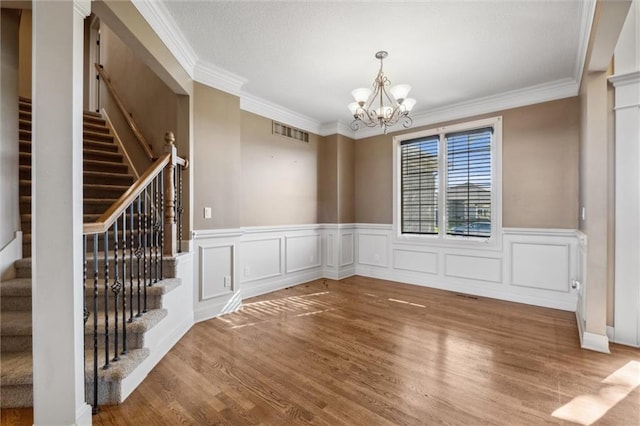 unfurnished dining area featuring stairway, wood finished floors, a chandelier, crown molding, and a wainscoted wall