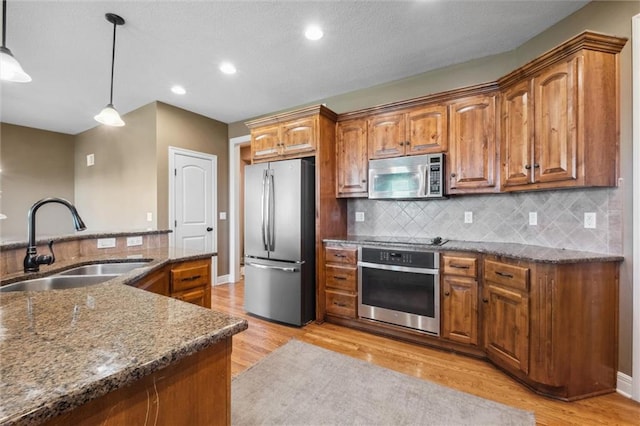 kitchen with stainless steel appliances, a sink, brown cabinets, dark stone countertops, and tasteful backsplash