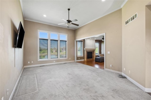unfurnished living room with a ceiling fan, ornamental molding, carpet, baseboards, and a fireplace