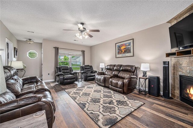 19204 E 15th Terrace Ct N, Independence, MO 64056 - living room featuring wood finished floors, a tile fireplace, a ceiling fan, a textured ceiling, and baseboards