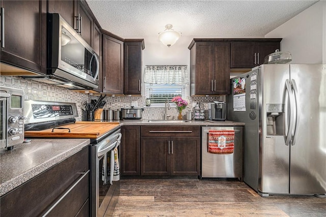 19204 E 15th Terrace Ct N, Independence, MO 64056 - kitchen with appliances with stainless steel finishes, a sink, dark brown cabinetry, tasteful backsplash, and dark wood-style floors