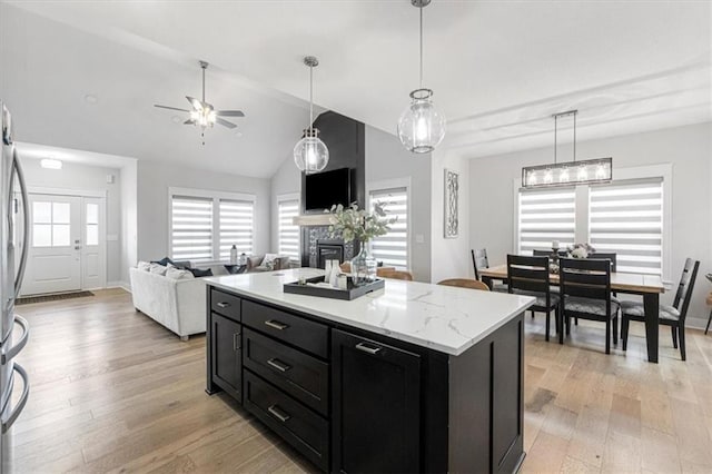 546 N Oakwood Ln, Tonganoxie, KS 66086 - kitchen with dark cabinets, a glass covered fireplace, light wood finished floors, ceiling fan, and pendant lighting