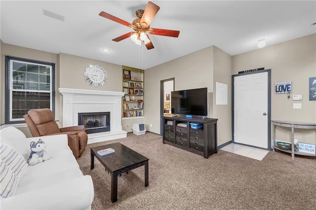 carpeted living area featuring ceiling fan, a fireplace with raised hearth, baseboards, and built in features