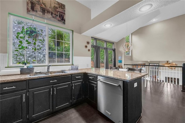 kitchen featuring stainless steel dishwasher, dark cabinetry, a sink, light stone counters, and high vaulted ceiling