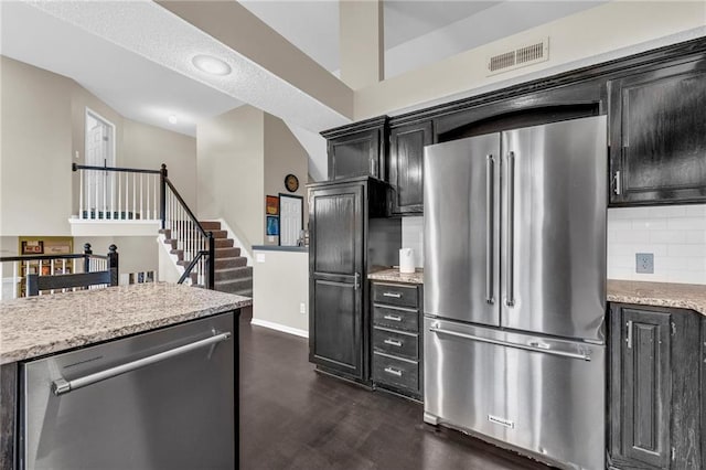 kitchen with stainless steel appliances, dark cabinets, tasteful backsplash, dark wood-type flooring, and baseboards