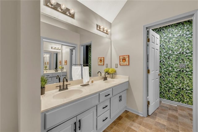 full bath with baseboards, lofted ceiling, double vanity, and stone finish floors