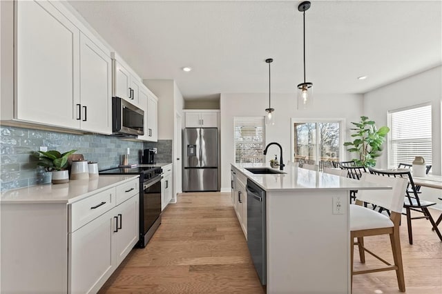 402 Woodview Dr, Raymore, MO 64083 - kitchen featuring appliances with stainless steel finishes, a sink, a kitchen bar, tasteful backsplash, and light wood-style floors