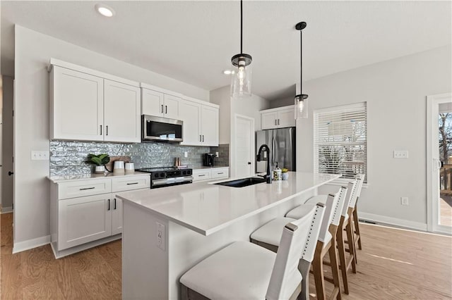 402 Woodview Dr, Raymore, MO 64083 - kitchen featuring stainless steel appliances, a sink, light wood finished floors, decorative backsplash, and a breakfast bar