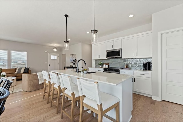 402 Woodview Dr, Raymore, MO 64083 - kitchen with stainless steel appliances, a sink, light wood finished floors, a breakfast bar area, and recessed lighting