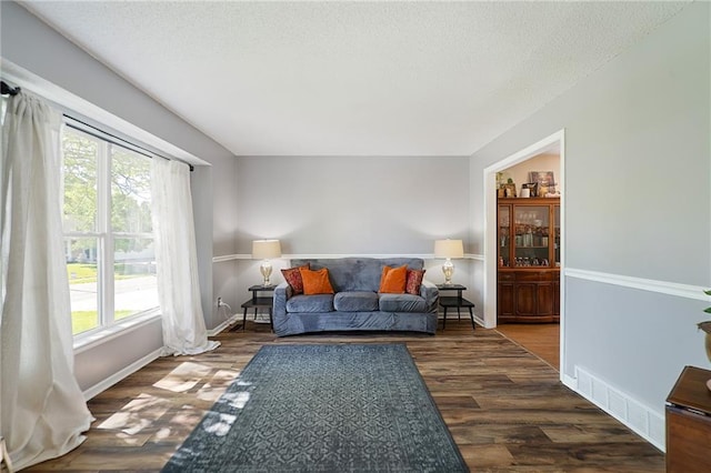 living area featuring healthy amount of natural light, dark wood finished floors, a textured ceiling, and baseboards