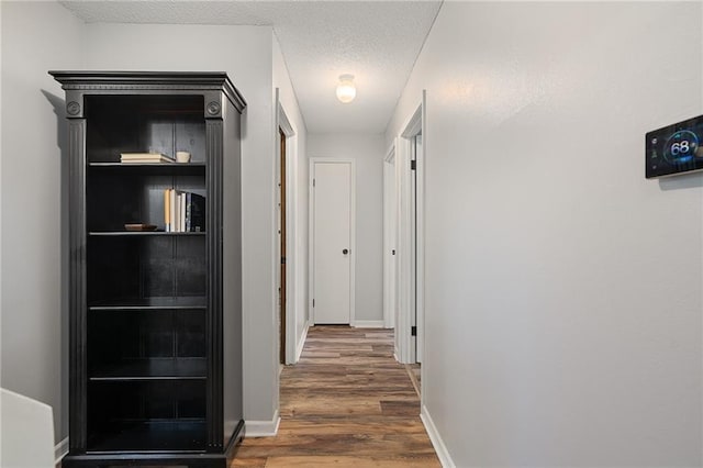 hall featuring wood finished floors, baseboards, and a textured ceiling