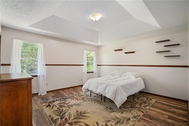 bedroom with multiple windows, wood finished floors, baseboards, and a textured ceiling