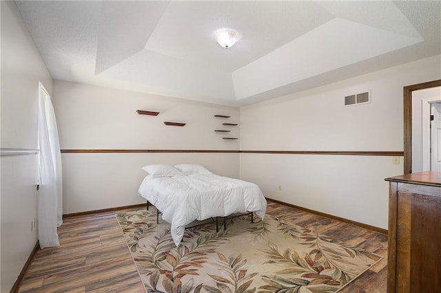 bedroom featuring a raised ceiling, wood finished floors, and baseboards