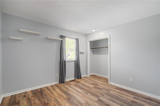 unfurnished bedroom with wood finished floors, a textured ceiling, baseboards, a closet, and recessed lighting
