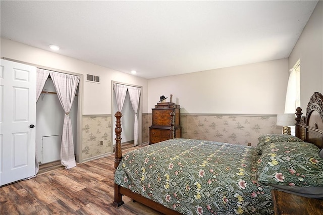 bedroom featuring wainscoting, wallpapered walls, wood finished floors, baseboards, and multiple closets