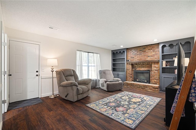 living area featuring a textured ceiling, wood finished floors, built in shelves, a brick fireplace, and a wainscoted wall