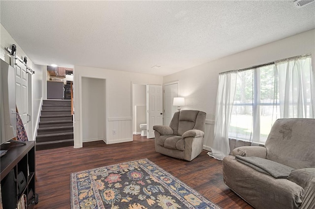 living room featuring a barn door, a textured ceiling, dark wood-style floors, and stairway