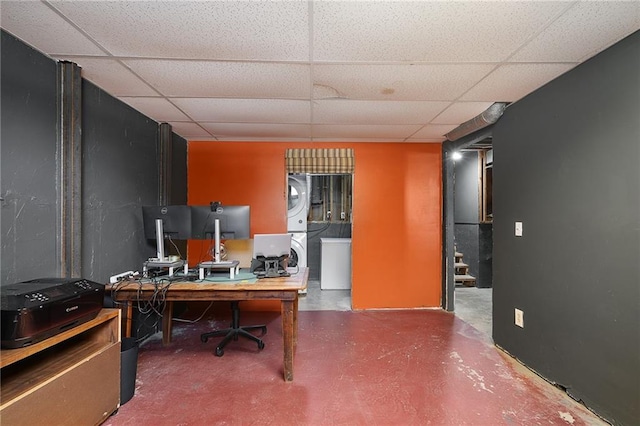 office with estacked washer and dryer, a drop ceiling, and concrete floors