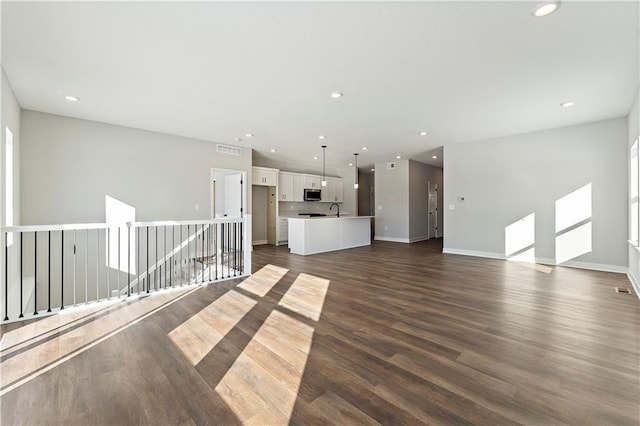501 Woodview Dr, Raymore, MO 64083 - unfurnished living room featuring dark wood-style flooring, baseboards, recessed lighting, and a sink