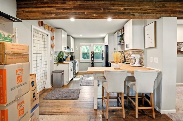 kitchen with black electric range oven, freestanding refrigerator, white cabinetry, a breakfast bar area, and baseboards