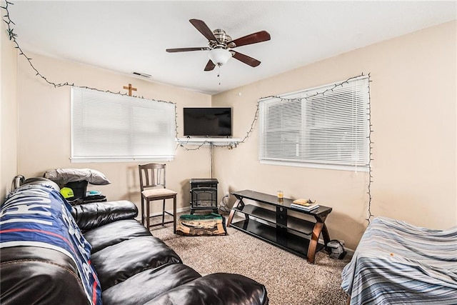 carpeted living area featuring a wood stove and ceiling fan