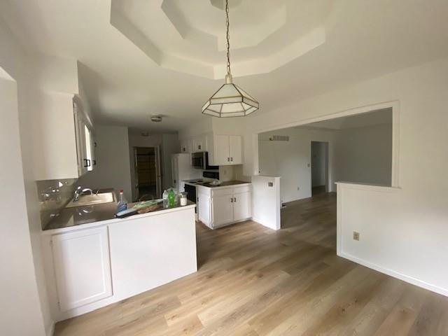 kitchen featuring a raised ceiling, white cabinets, light wood-style floors, a peninsula, and baseboards